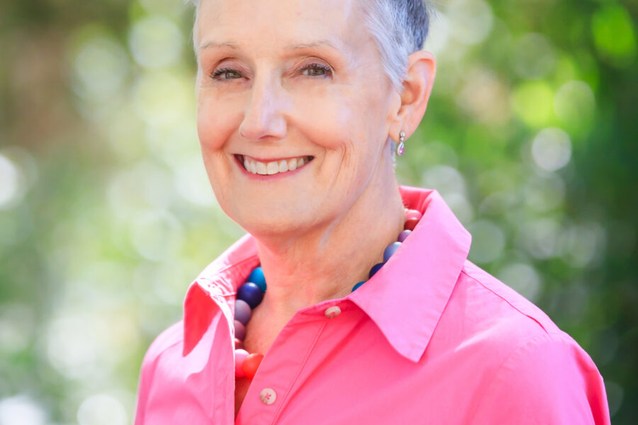 portrait of Kim Bedier, CVE, in vibrant pink shirt, in front of green landscape